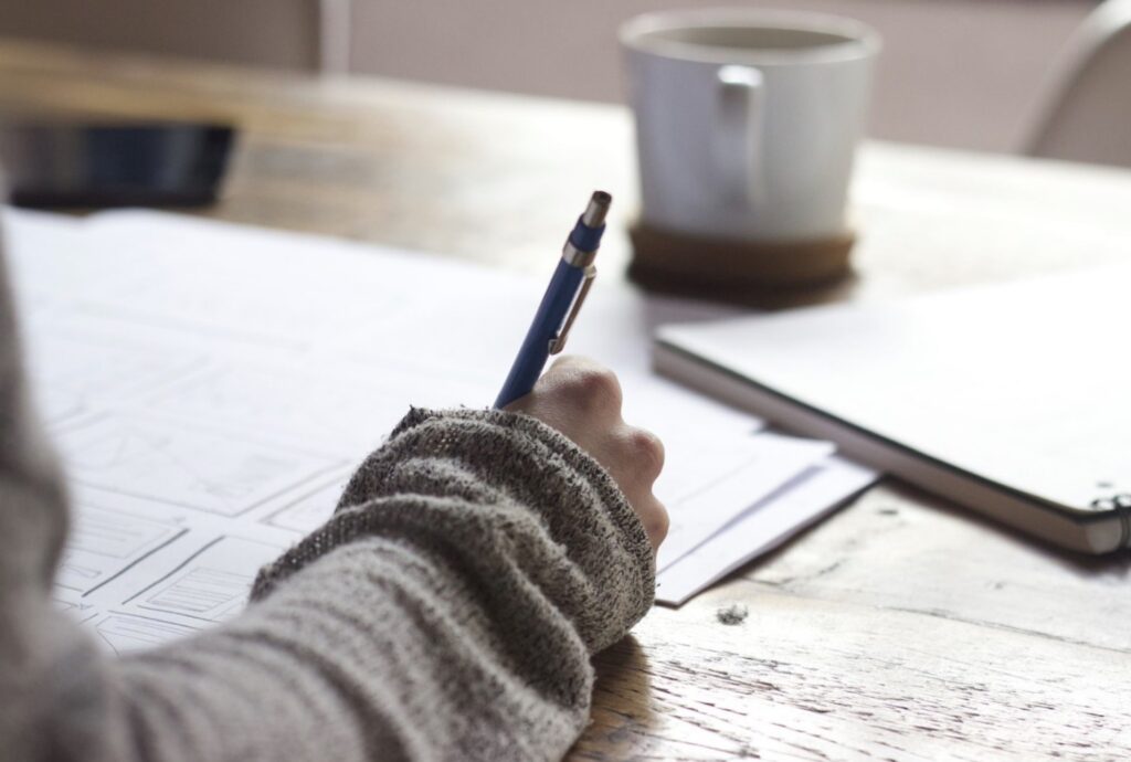 Person writing, papers, note pad and a coffe mug